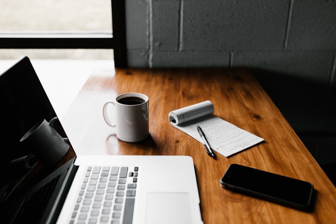 A laptop, coffee cup and notepad on a wooden desk while files are converted online